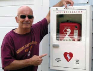 Joe standing next to an AED, the device that saved his life.