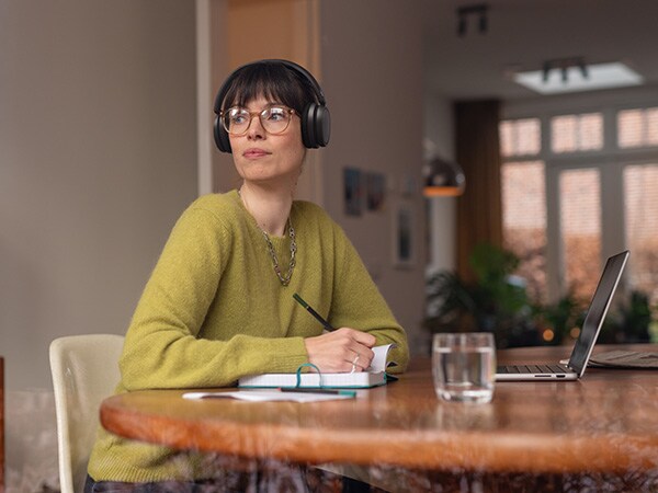 Isik, kes kannab mugavaid Philipsi kõrvaklappe, istub laua taga, kus on märkmik ja sülearvuti