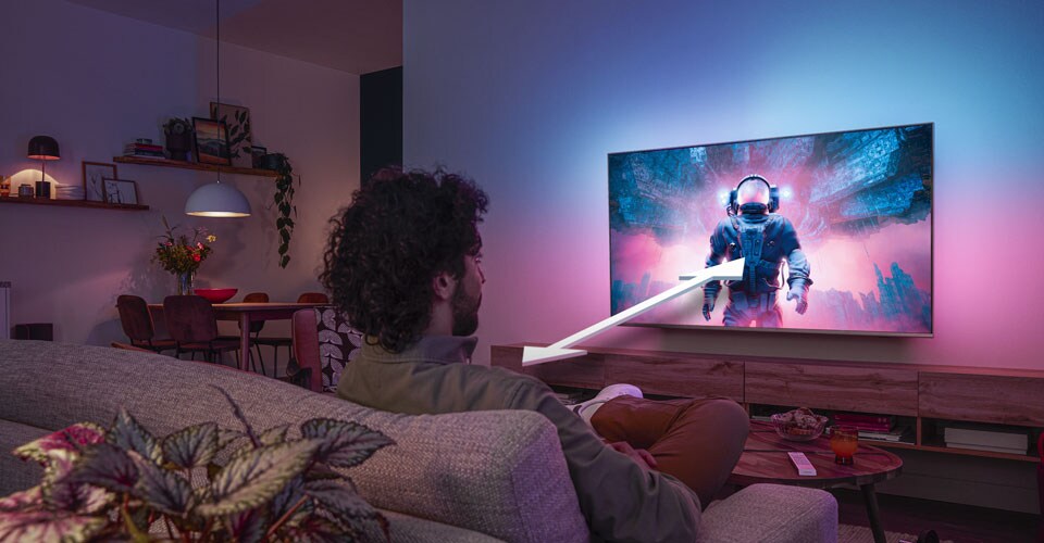 Mees istub diivanil ja vaatab Philipsi Ambilight-telerit, millel on kujutatud värvilist astronaudistseeni, mille nool näitab optimaalset vaatamiskaugust