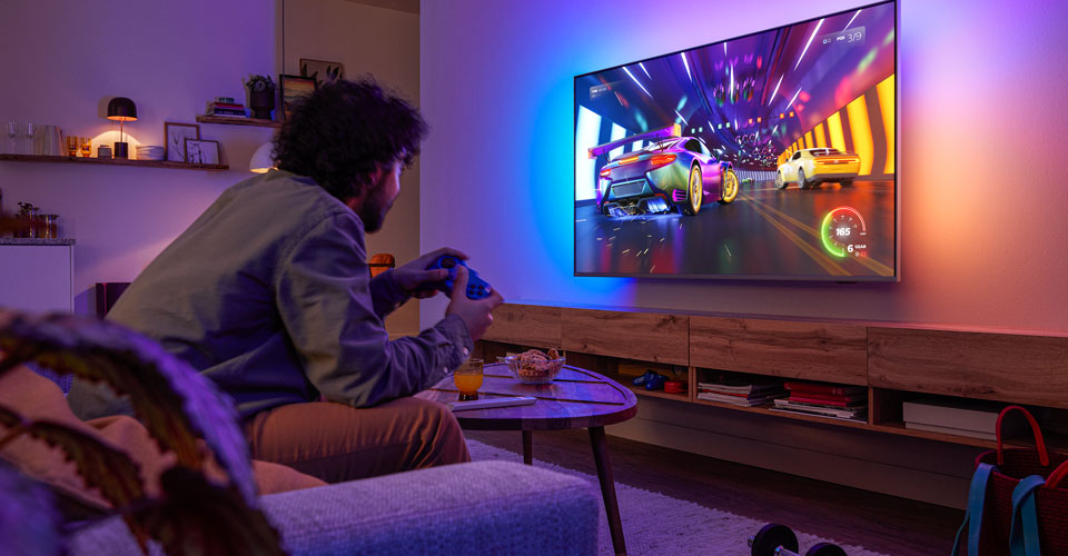 Inimene istub diivanil ja mängib Philipsi Ambilight-teleril võidusõidumängu